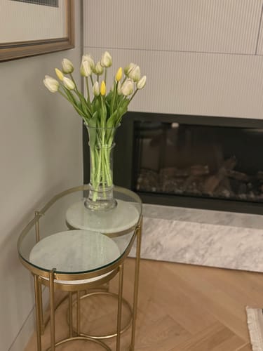 Customer's white and yellow tulips arranged in a clear vase on a side table.