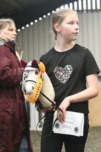 Reviewer holds a hobby horse wearing the red ear bonnet, decorated with a fifth place ribbon.
