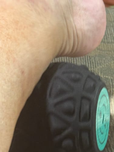 Close-up of a customer using the black Vibit ROLL massage roller on their ankle.