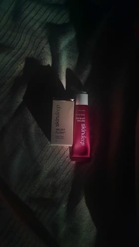 Reviewer's dimly lit photo of the Lip Glaze+Velvet Flush Duo, showing the blush box and red lip glaze tube on a dark surface.