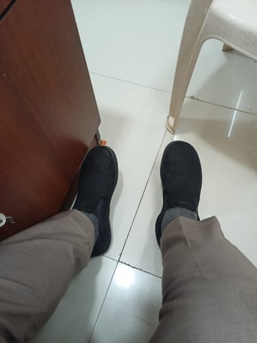 Customer's point-of-view showing their feet in a pair of black slip-on Frido shoes on a tiled floor.