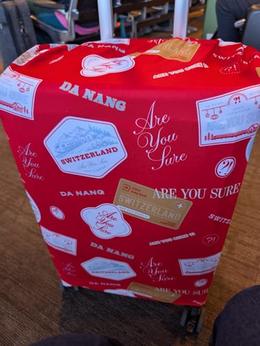 Customer's red patterned BTS luggage cover fitted over a suitcase, with the handle extended through the top opening.