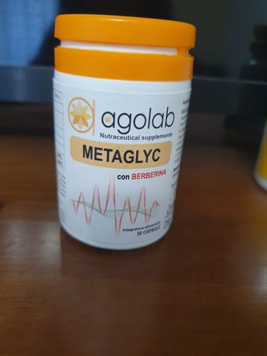 Il cliente mostra il flacone bianco dell'integratore Metaglyc con tappo arancione, appoggiato su un tavolo.