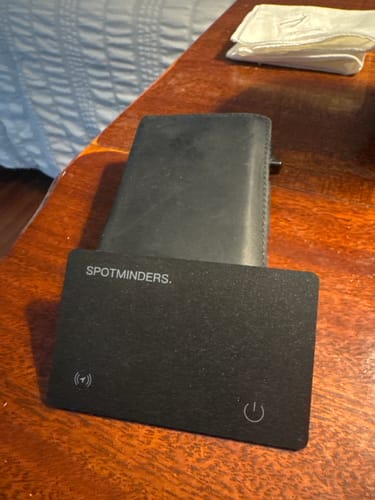 Customer's black SPOTMINDERS Tracking Card resting against a wallet on a wooden table.