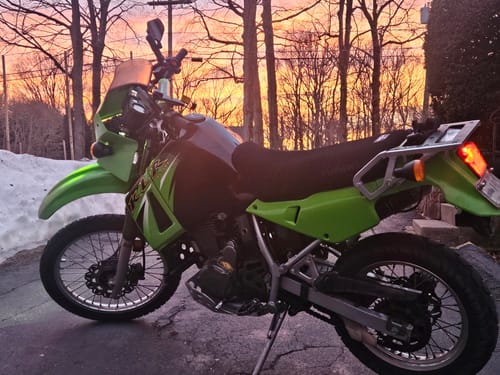 Reviewer's black Wind Rider Seat Cover installed on a green and black motorcycle at sunset.