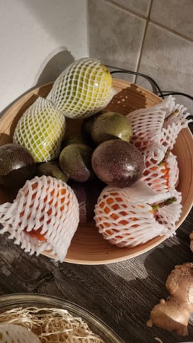 Ein Kunde zeigt seine Früchte aus der Mango-Träume Mix-Box in einer Holzschale, einige davon sind in weißen Schutznetzen.