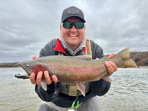 Reviewer smiling while holding a large, colorful trout caught on the river.