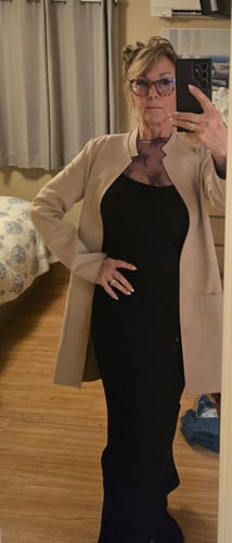 Reviewer in a bedroom wearing the black Maxi Shapewear Dress, layered under a beige jacket.