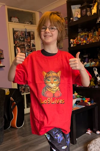 Reviewer's son smiling and giving two thumbs up while wearing the red Kids soft t-shirt with a cat graphic.