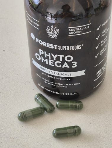 Customer's bottle of Phyto Omega 3 with several dark green vegan capsules in front.