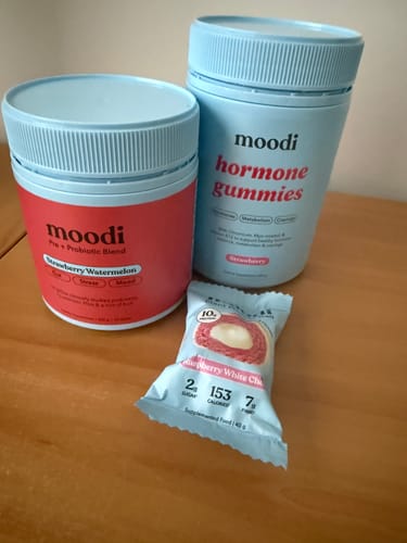 Customer's red tub of Strawberry Watermelon Pre + Probiotic Blend, shown with hormone gummies and a protein ball.