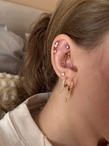 Customer displays their ear after the Custom Styling Service, showing a curated stack of gold and crystal earrings.