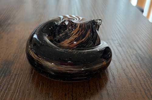 Reviewer's beautiful, swirled glass Spirit Piece in the shape of a curled pet, resting on a wooden table.