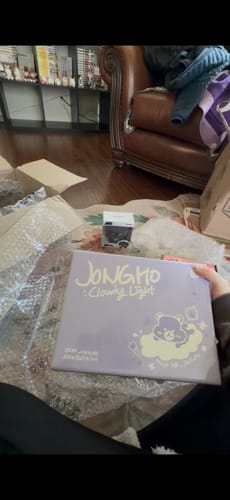 Reviewer holding a purple Jongho merchandise box from their K-POP RANDOM BOX, with packaging on the floor.
