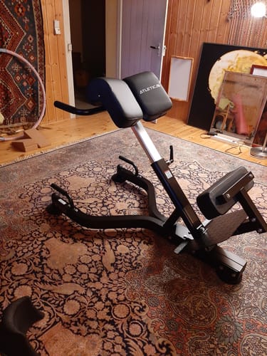 Rezensent zeigt die aufgebaute schwarze Hyperextension, die stabil in einem Wohnzimmer steht.