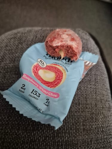 A customer's Raspberry White Choc Plant Protein Ball with a bite taken out, revealing the white center as it rests on its packaging.