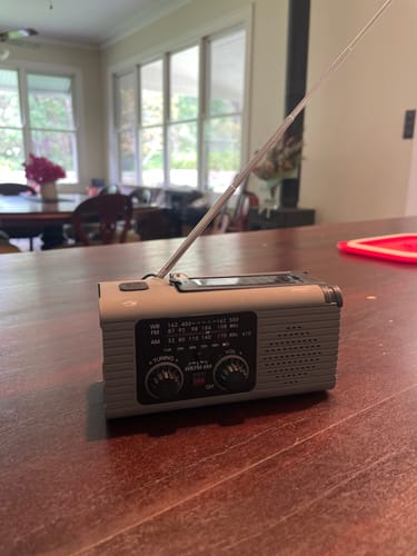 Customer's grey All-in-One Emergency Weather Radio on a wooden kitchen table with its antenna extended.