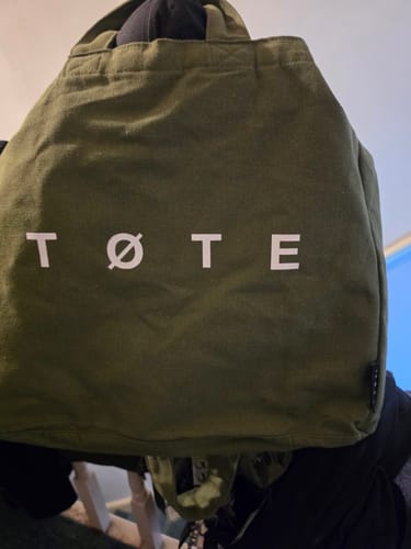 Customer's Khaki Green TØTE Bag hanging indoors, showing the white logo on the front.