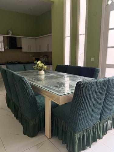 A customer's dining room featuring dark green fitted bubble chair covers on chairs around a glass-topped table.