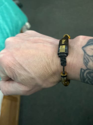 Reviewer's wrist wearing the Nighthawk Tiger's Eye Bracelet, showing a close-up of the black clasp with gold design.