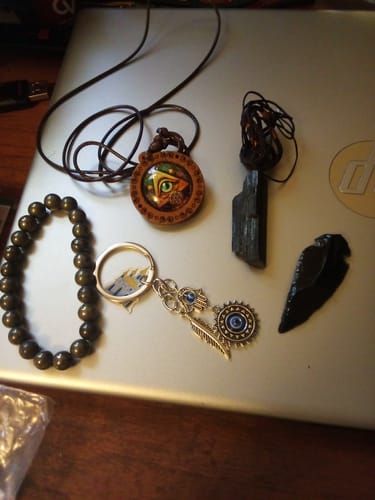 Reviewer's AuraBloom Subscription Box contents, including two necklaces, a bracelet, a keychain, and a stone, laid on a laptop.