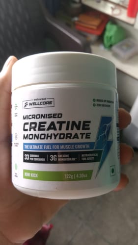 Customer holding a white tub of Wellcore Micronised Creatine Monohydrate in the Kiwi Kick flavor.