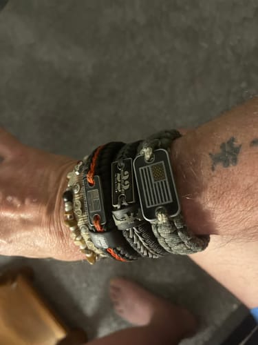 Reviewer's wrist stacked with several patriotic bracelets, including the braided 22 A Day Paracord Bracelet.