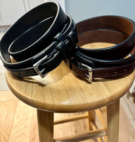 Reviewer's black and brown The Ranger belts coiled on a wooden stool.