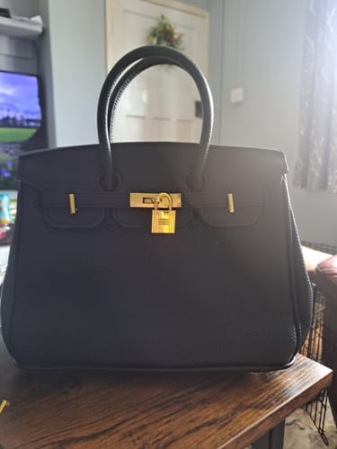 Customer's black pebbled Warkin Bag with gold hardware, sitting on a wooden table.