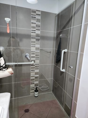 Customer shows a spotless glass shower door with a dark KoalaCloth LITE hanging inside, demonstrating the clean results.