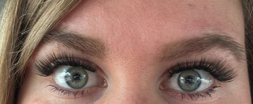 Kundin zeigt in Nahaufnahme ihre Augen mit langen, vollen Wimpernextensions.