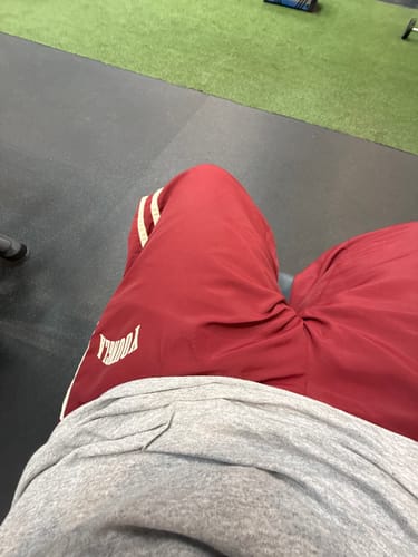 Close-up of a customer wearing the red Flagship Track Pants with white stripes while sitting at a gym.