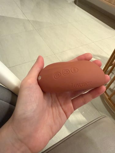 Customer holding the terracotta-colored Lovemere Warming Lactation Massager in their palm, showing the control buttons.