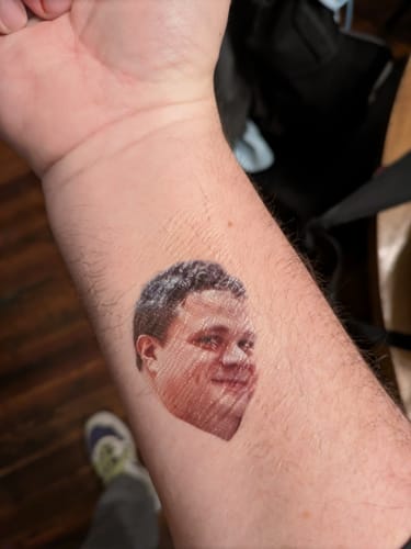 Customer's forearm with a clear custom photo temporary tattoo of a man's face for a bachelor party.