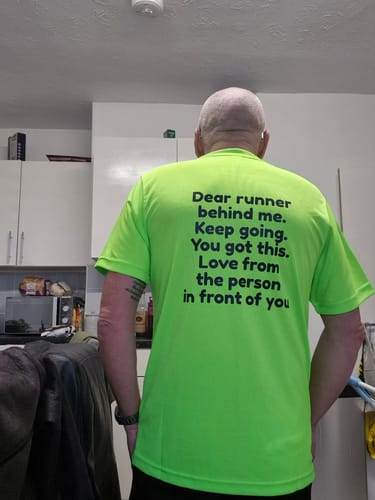 Customer shows the back of their bright green technical t-shirt with a motivational print.