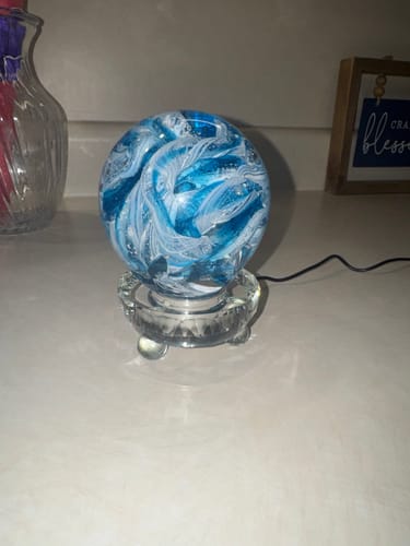 Reviewer's swirled blue Cotton Candy Orb with Ash in Glass displayed on a clear glass stand on a countertop.