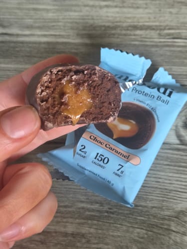 Reviewer holds a bitten chocolate protein ball, showing its gooey caramel filling.