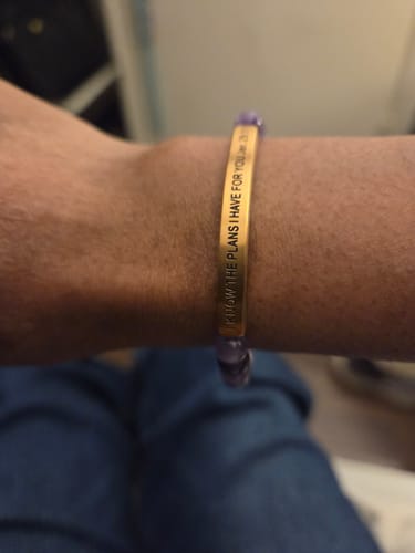 A reviewer's wrist wearing the gold engraved 'I KNOW THE PLANS I HAVE FOR YOU' faith bracelet.