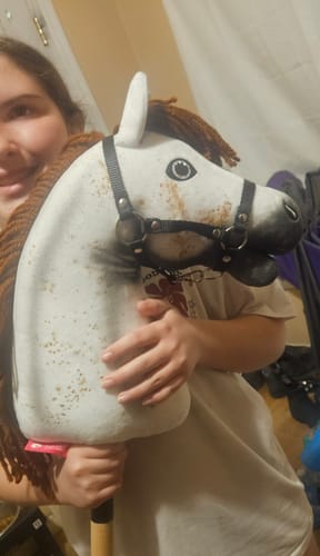 A customer smiling while holding the white, spotted Hobby Horse Rufus with a black halter.