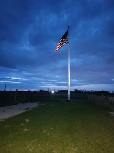 Reviewer's Ultra Heavy Duty American Flag illuminated on a flagpole against a cloudy dusk sky.