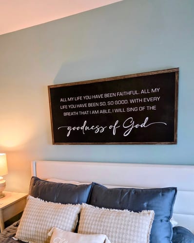 Reviewer's Goodness Of God Faith Sign II hanging on a bedroom wall above a bed.