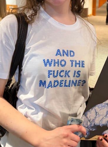 Customer wearing a white Everyday tee with the blue text 'AND WHO THE FUCK IS MADELINE?'