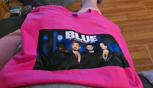 Customer's bright pink soft t-shirt featuring a custom print for the band Blue's 25th Anniversary Tour, laid out on a lap.