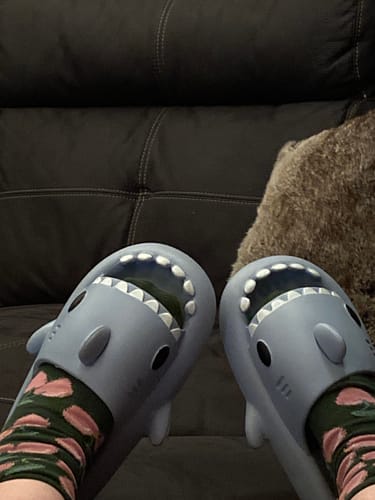 Customer relaxing on a couch while wearing grey Cloud Sharks slides over patterned socks.