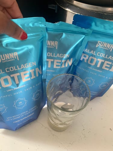 Reviewer with three blue pouches of a collagen protein supplement and a glass of water.