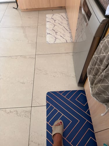 Reviewer's two Anti-Fatigue Standing Mats on a kitchen floor: one blue geometric mat and one white marble mat.