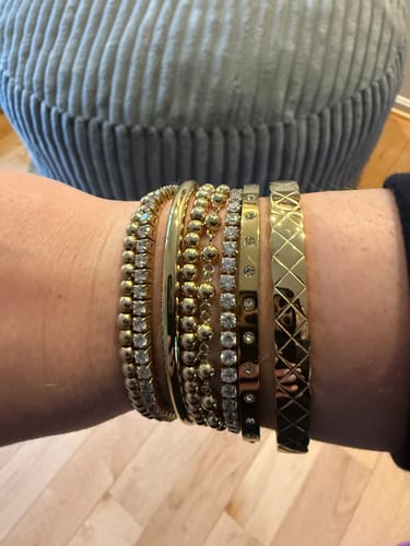Customer's wrist showing the Classic Oval Bangle worn in a stack with other gold bracelets.