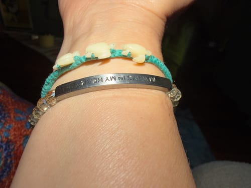 Close-up of a reviewer's wrist wearing the engraved 'Always In My Heart' bracelet stacked with a teal turtle bracelet.