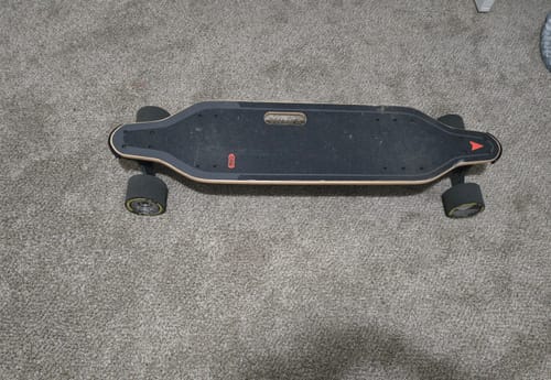 Customer's refurbished skateboard viewed from the top, showing the black deck with wooden edges on a carpet.