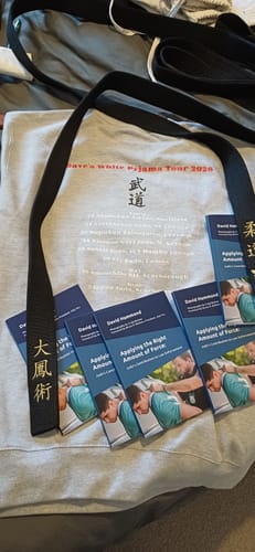 Reviewer's grey sweater with custom printing for a martial arts tour, shown with a black belt and books.